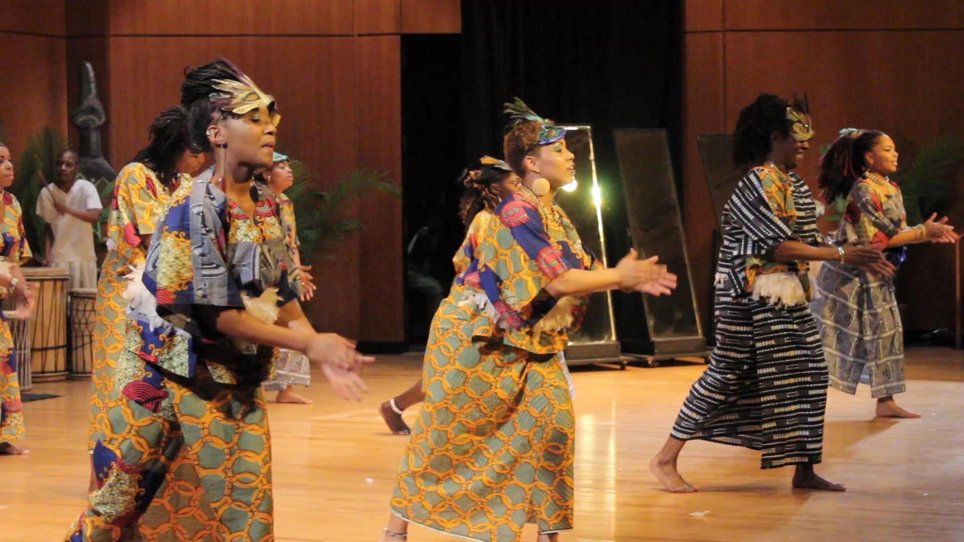Group of women in colorful African attire dancing on stage.