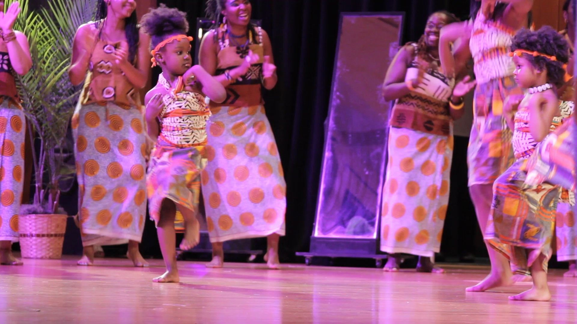Group of people dancing on stage in traditional African attire.