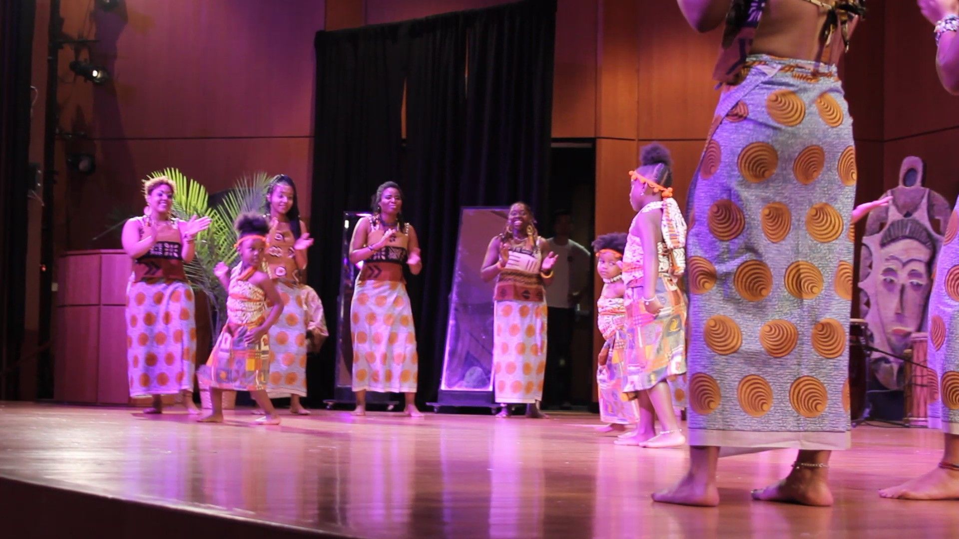 People in colorful outfits perform on a stage, dancing and smiling.