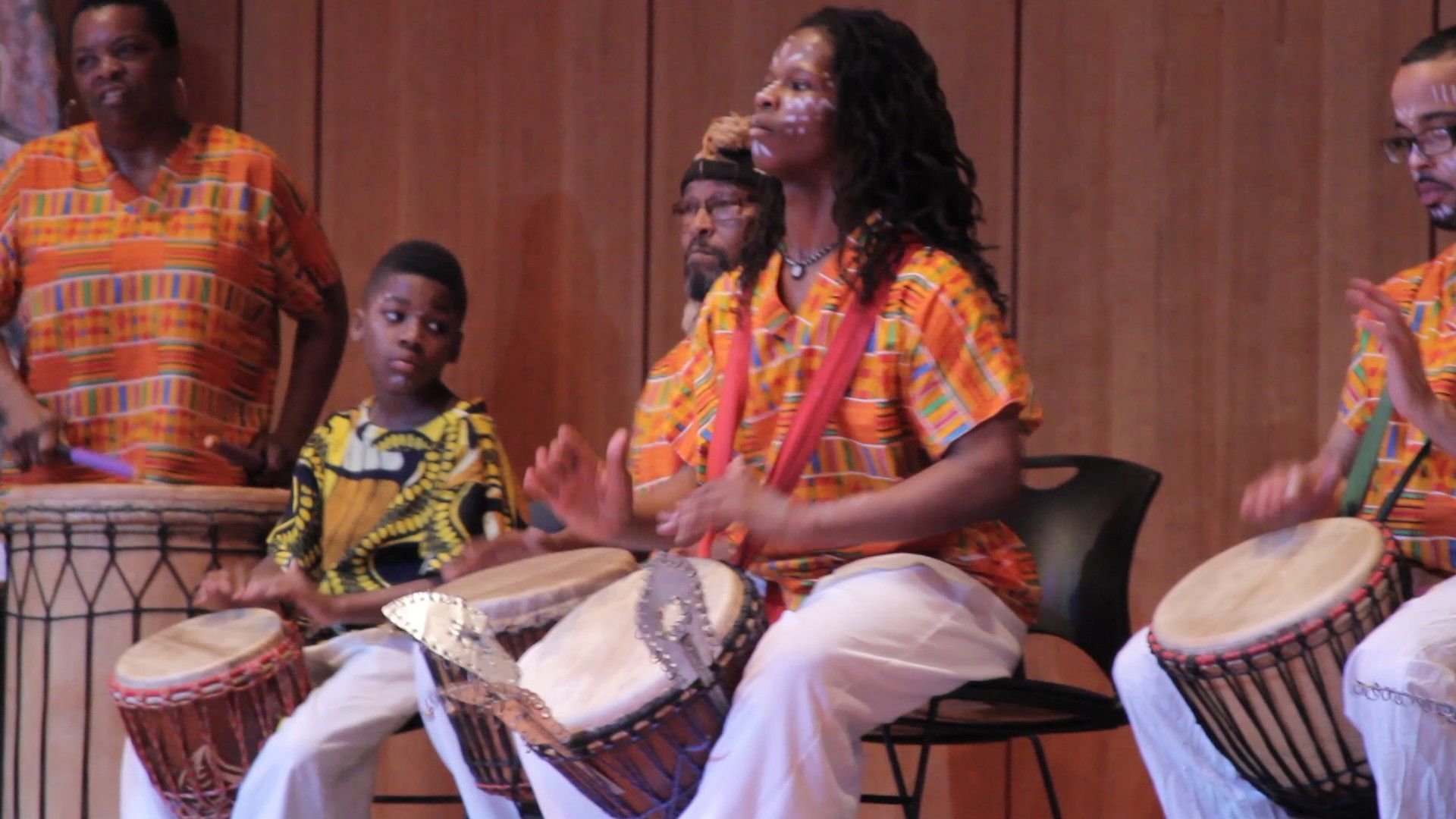Group of people playing drums in colorful African attire, indoors.