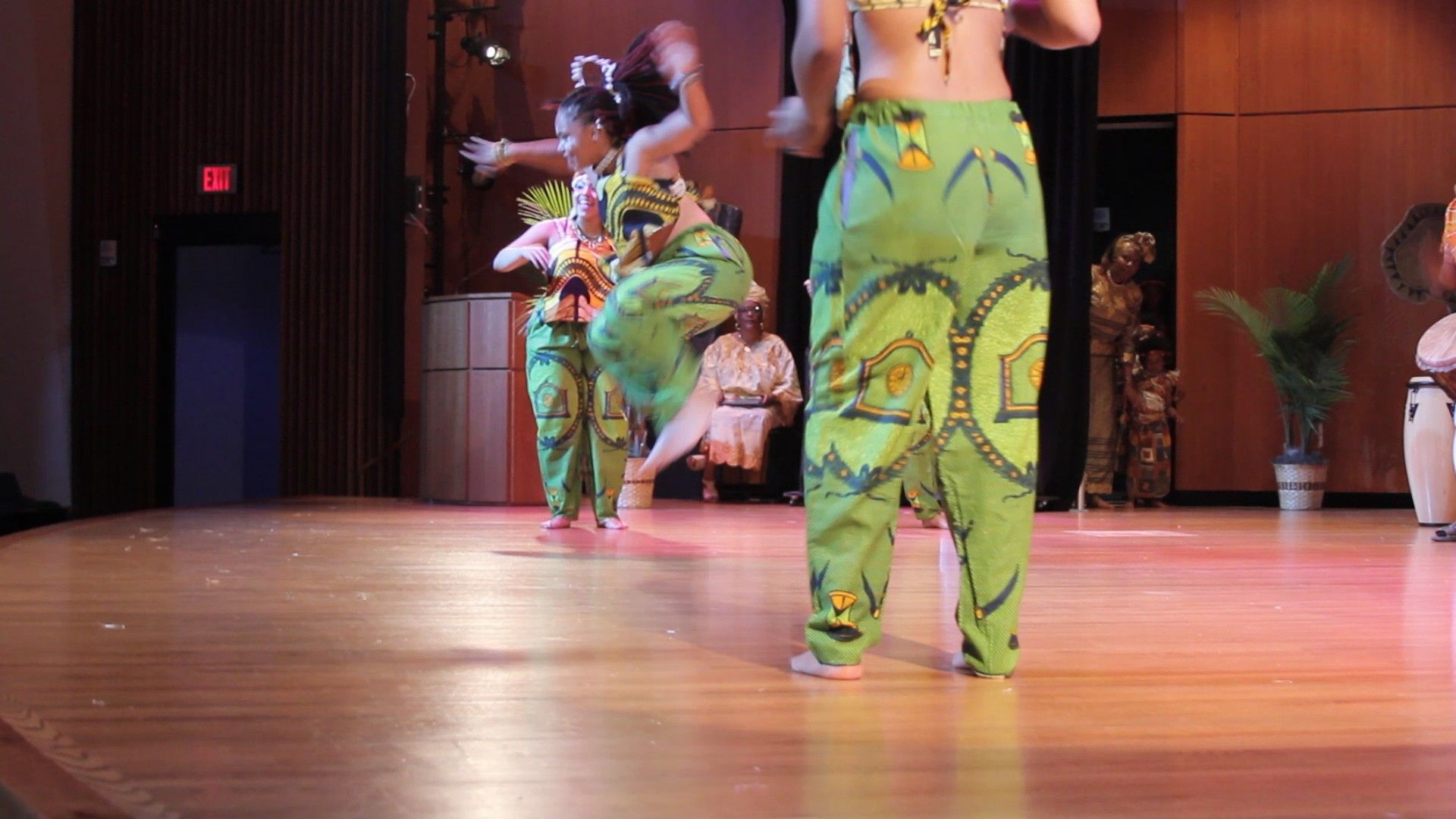 Women in green patterned outfits dance on stage.