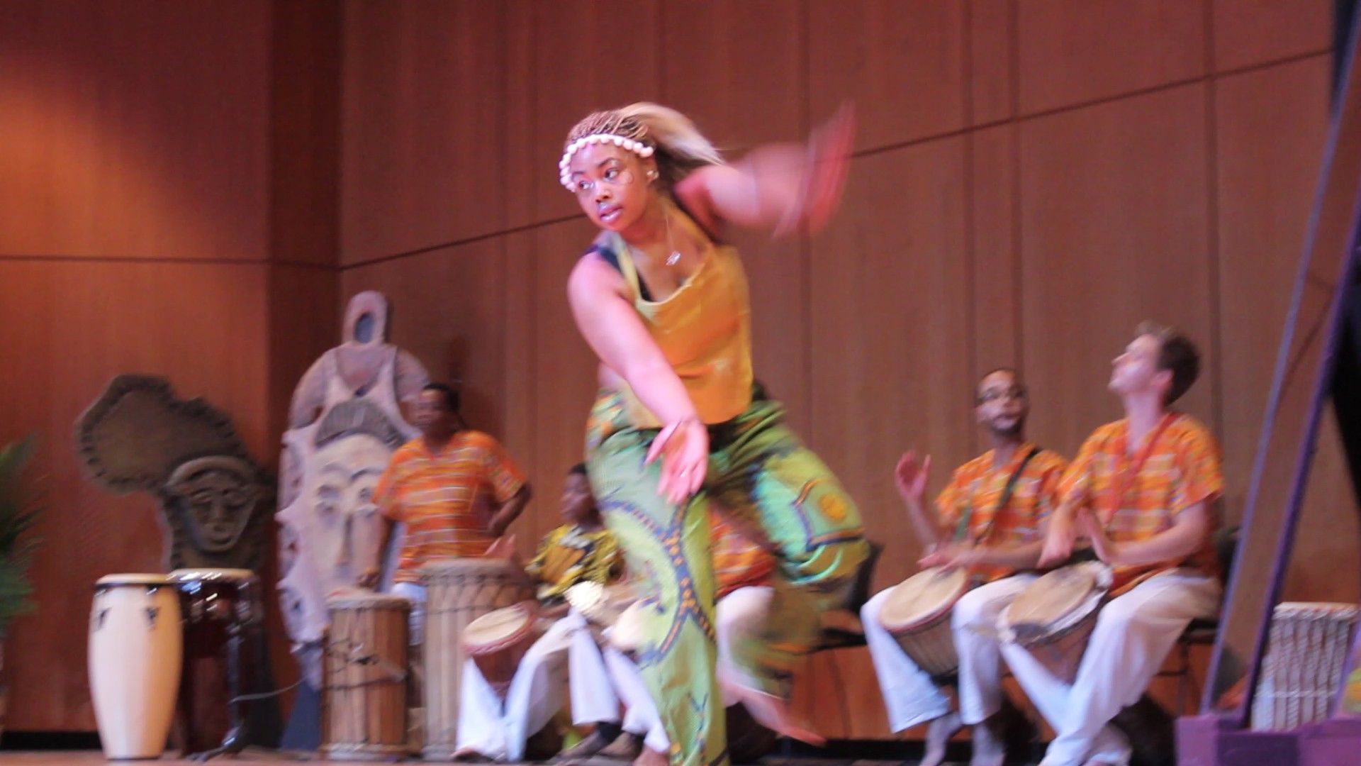 Woman dances energetically on stage, with a band of drummers in the background.