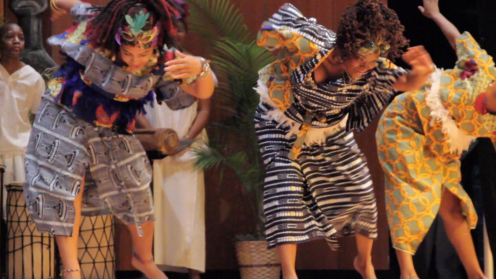 People dancing in colorful African-style attire. Stage performance with movement and energy, dark background.