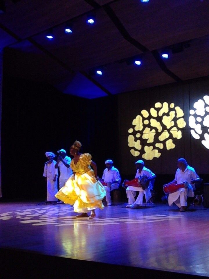 A woman in a yellow dress dances on stage with musicians in white, under blue lights.