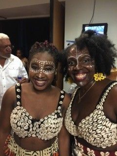 Two women in shell-decorated tops, face paint, smiling, and posing for a photo.