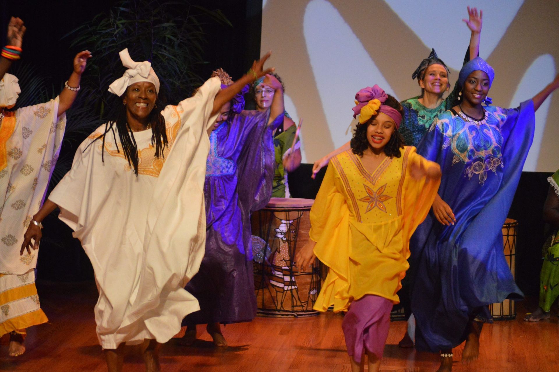 People in colorful African attire dancing on a stage, arms raised.