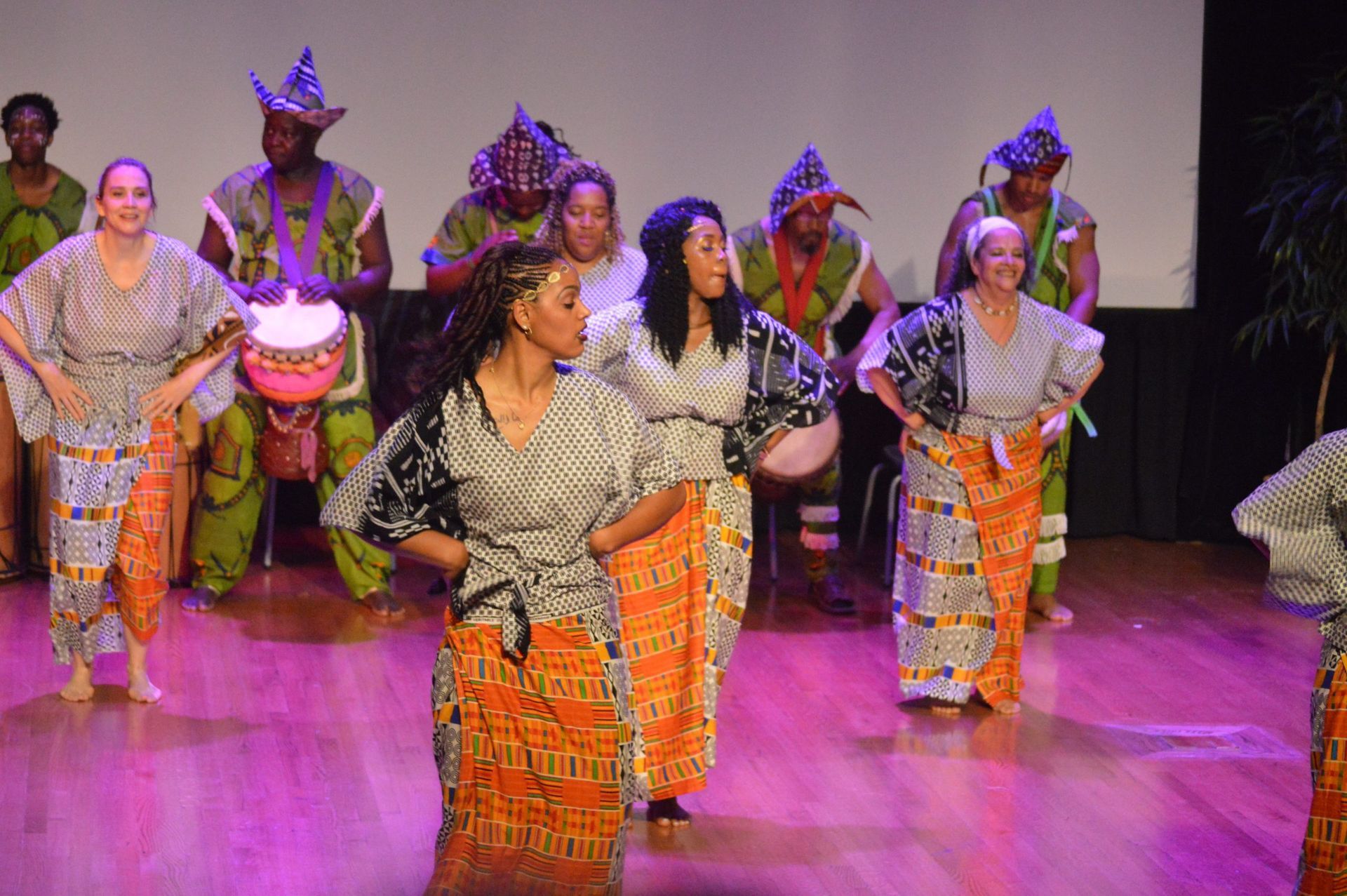 Group of people performing a dance on stage, wearing colorful traditional attire.
