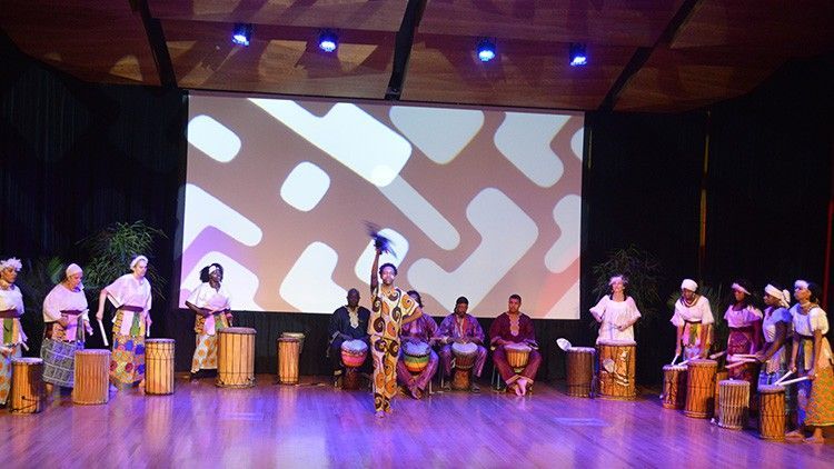 African dance and drum performance on stage, with performers in traditional dress.