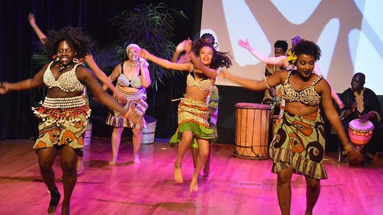 Dancers in colorful outfits performing on stage with drummers in the background.