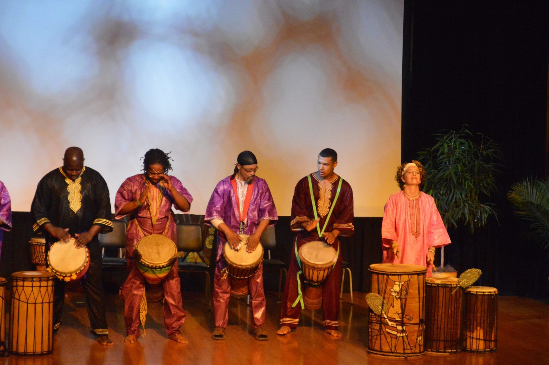 Group of people in colorful robes playing drums on stage.