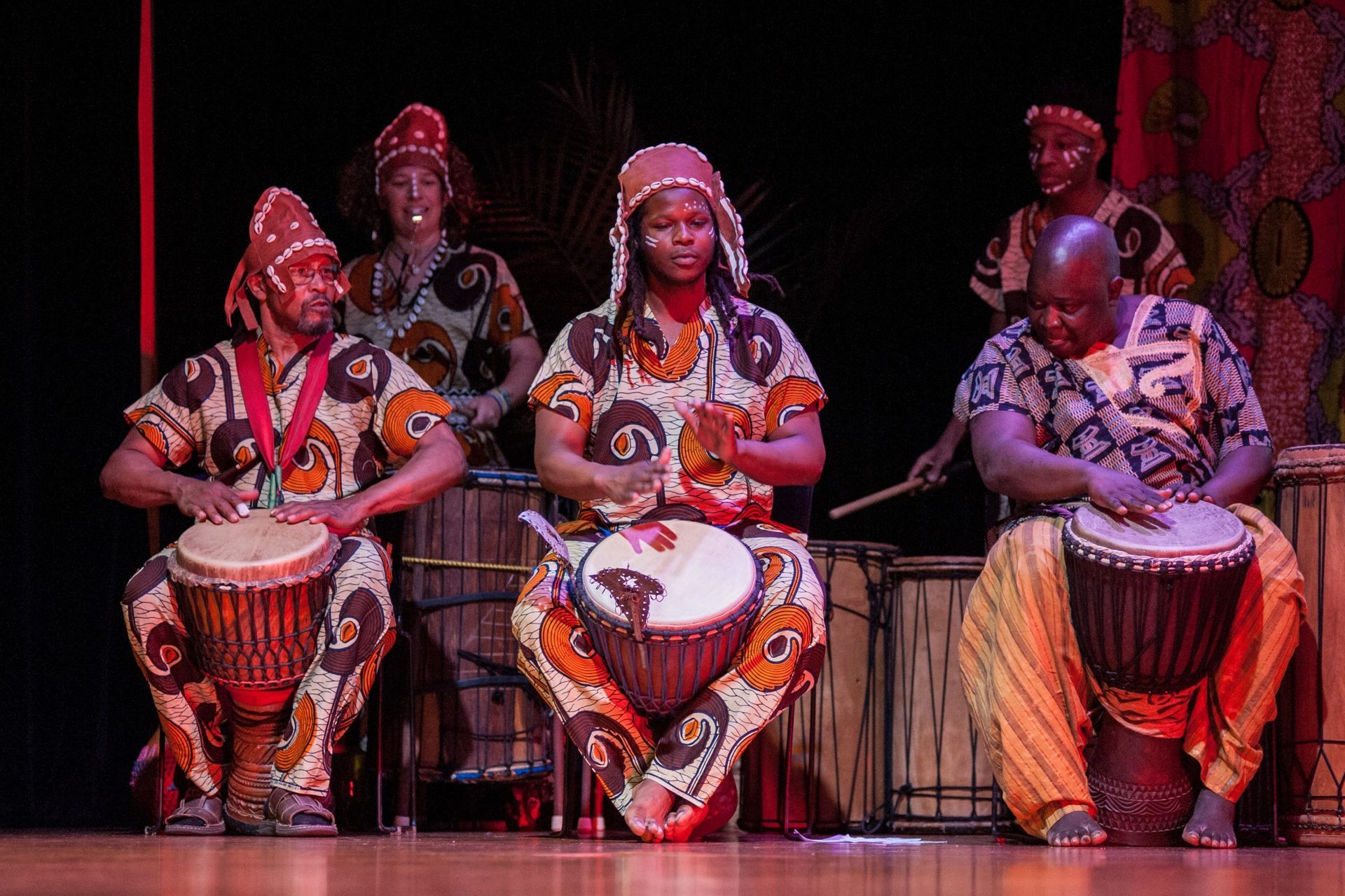 People in colorful African attire play drums onstage.