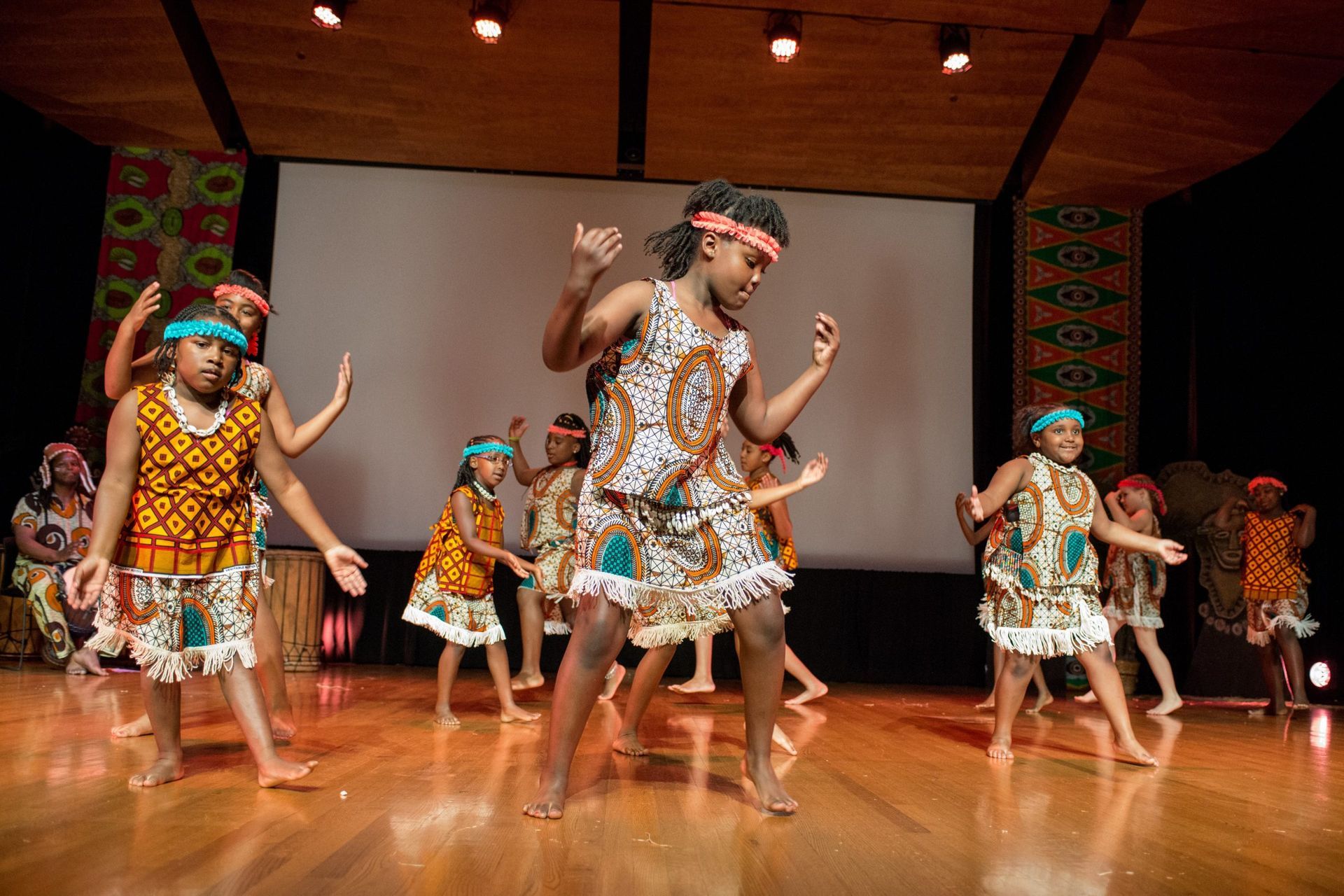 Children in colorful African-style outfits dancing on a stage.