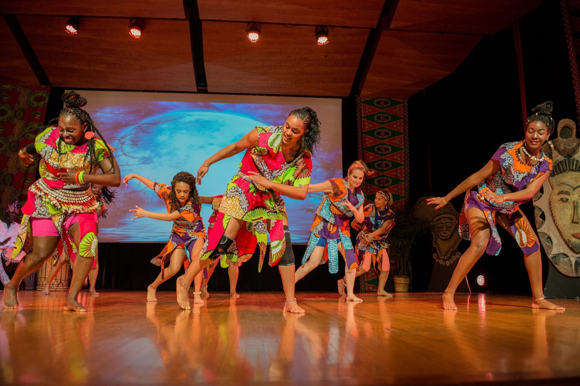 Group of dancers in colorful African print outfits performing on stage.