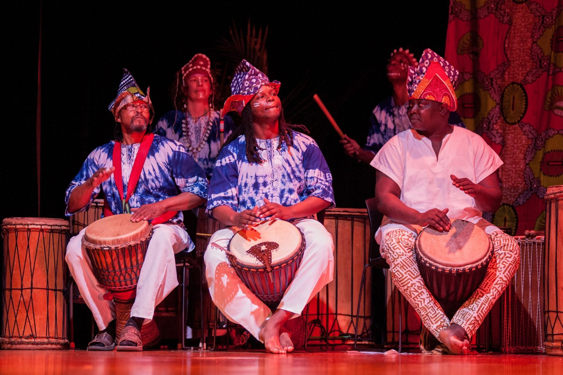 A group of people playing drums on stage, dressed in colorful African attire.