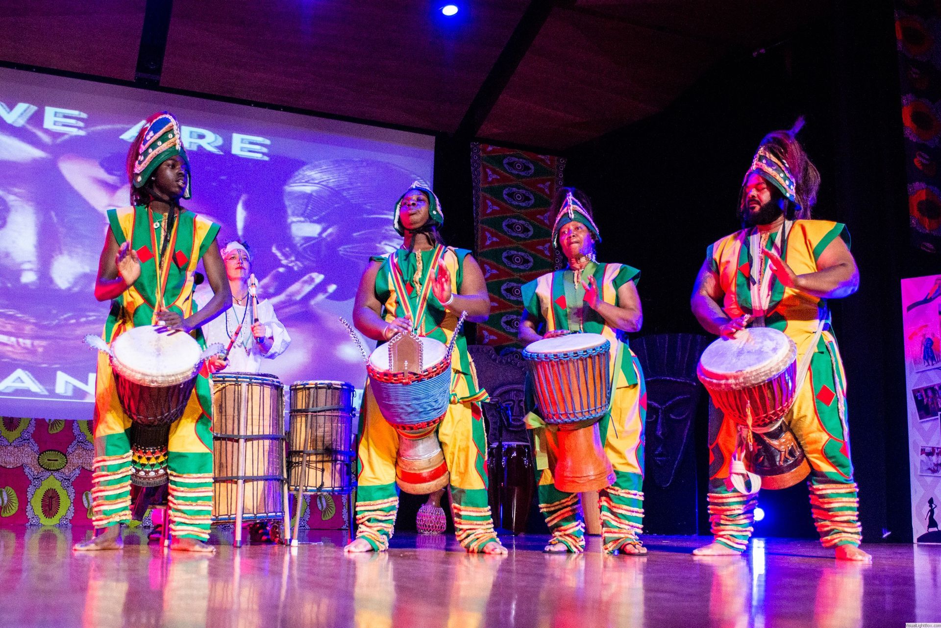 Four drummers in colorful African attire play their instruments on stage.