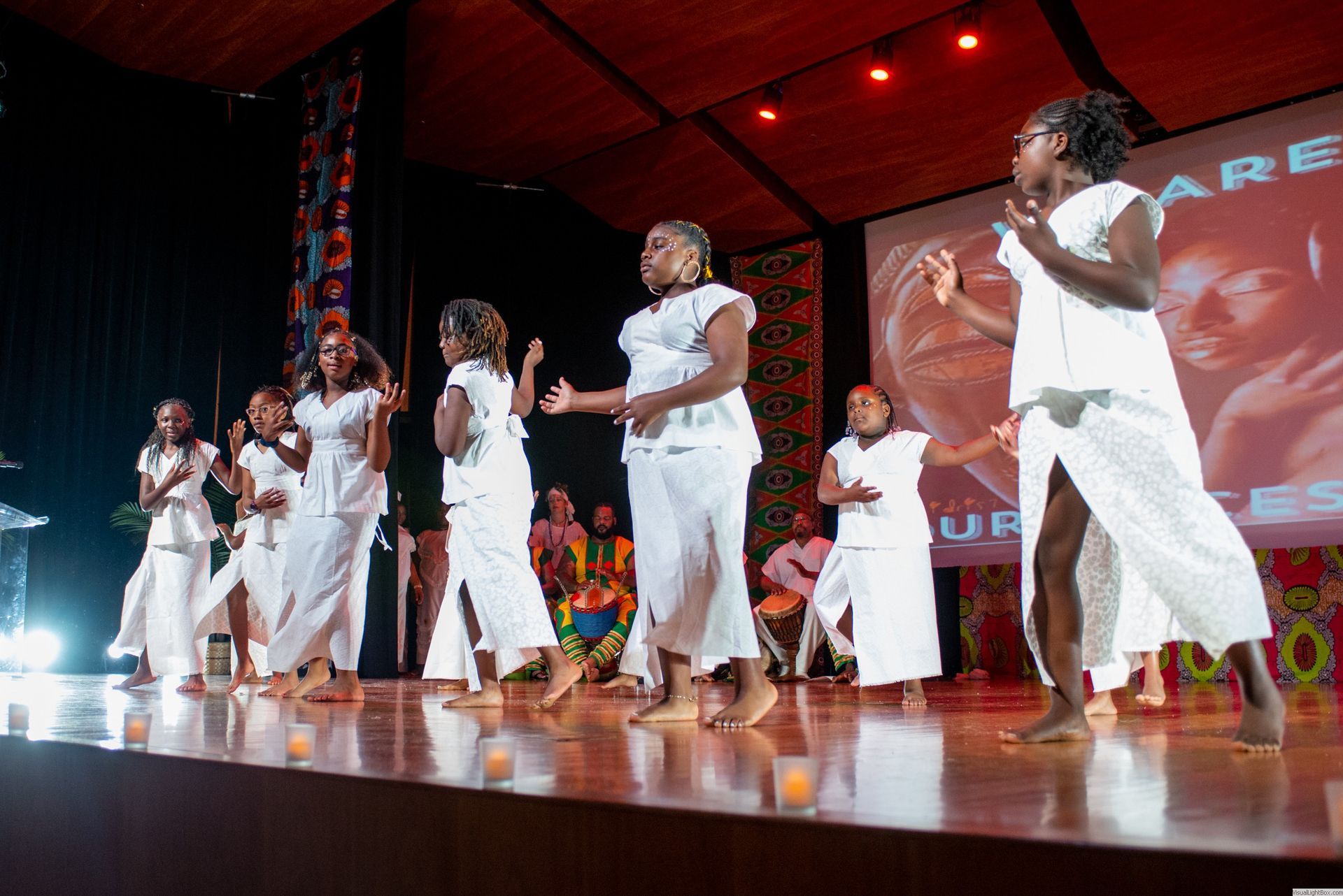 Group of people in white outfits dancing on stage at an event.