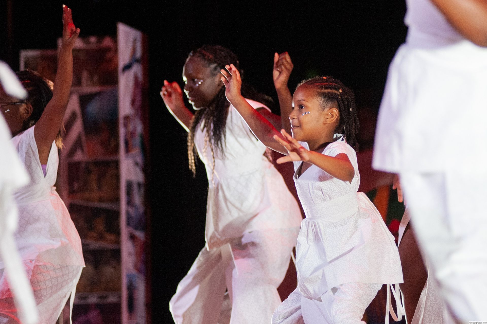 Dancers in white outfits perform outdoors at night; a woman and child are the focus.
