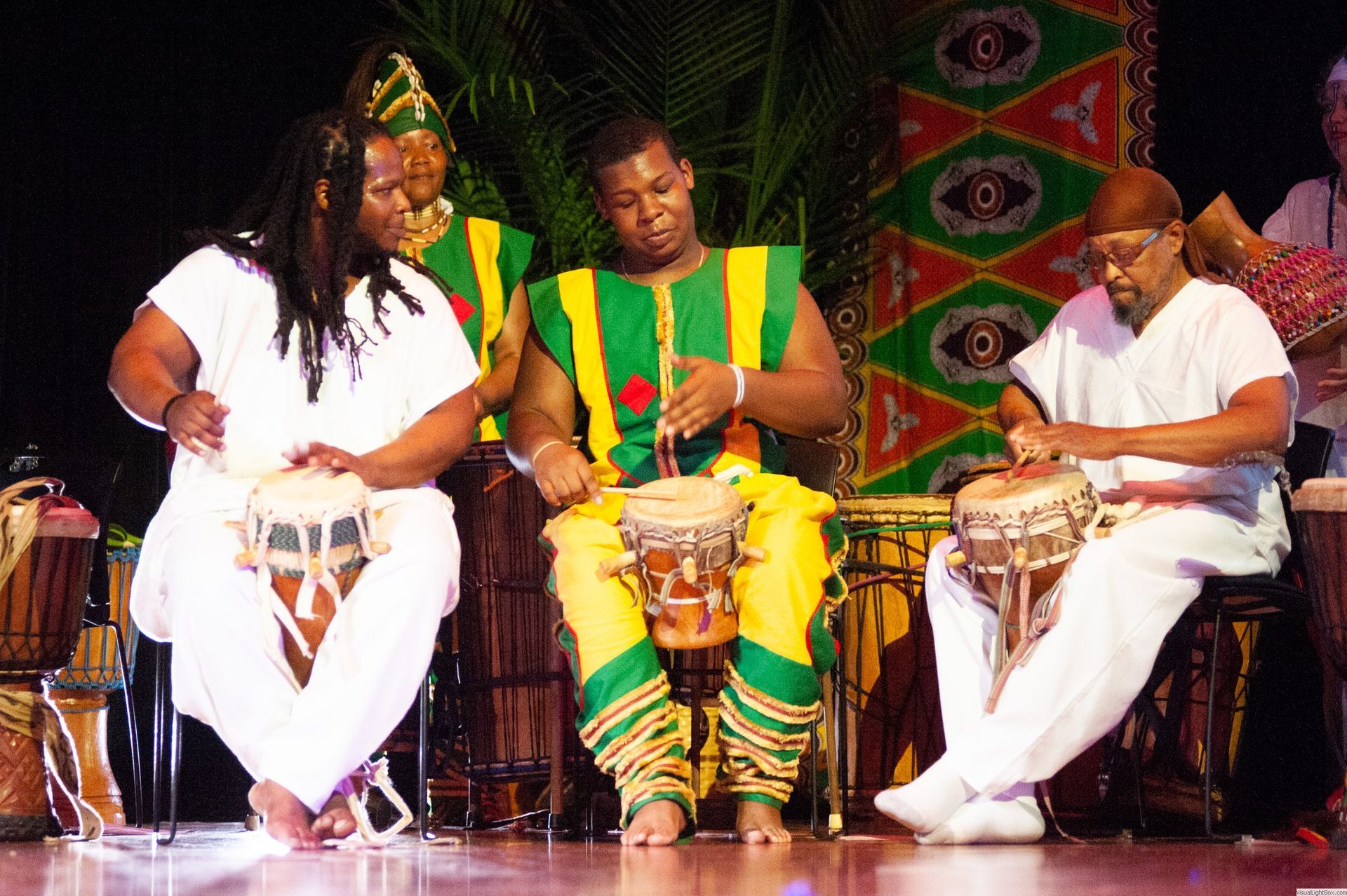 Drummers in white and green outfits playing drums on stage.