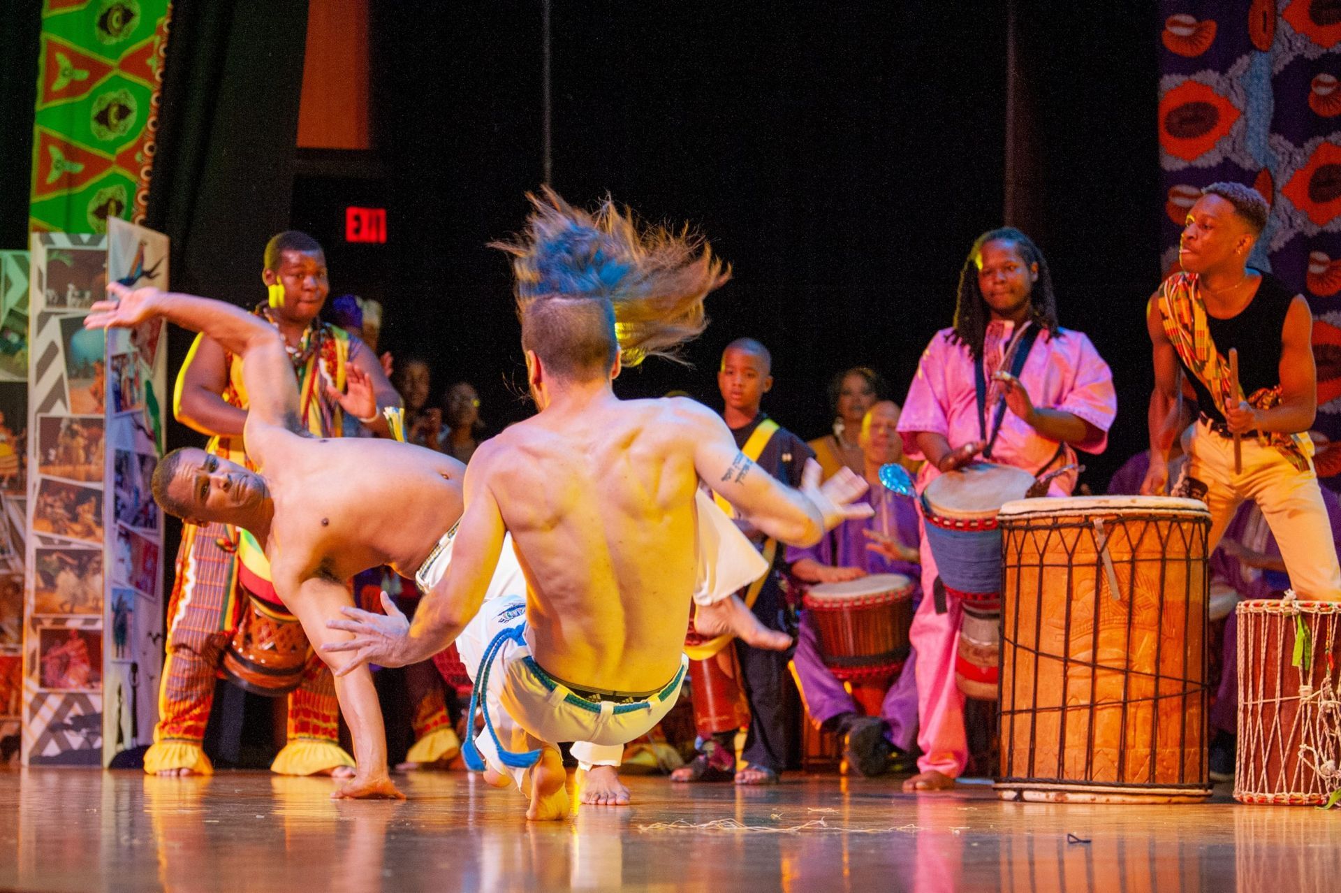 A group of African drummers and dancers on a stage. Dancers are performing acrobatic moves.