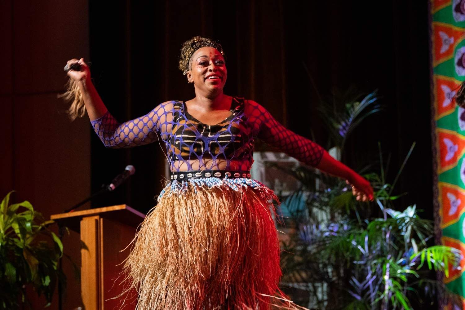 Woman in traditional attire dances on stage, arms raised.