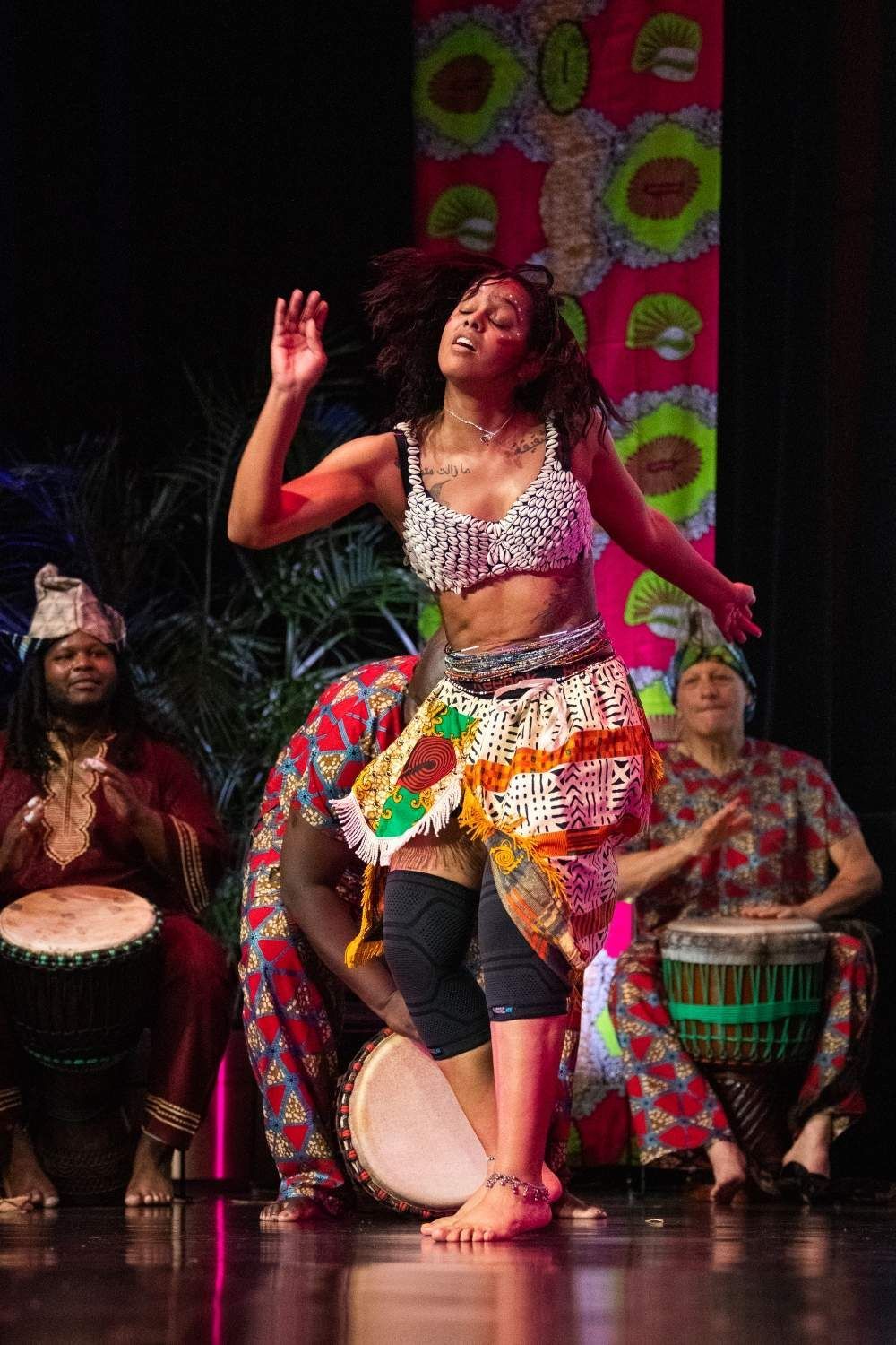 Woman dances energetically on stage in front of drummers.