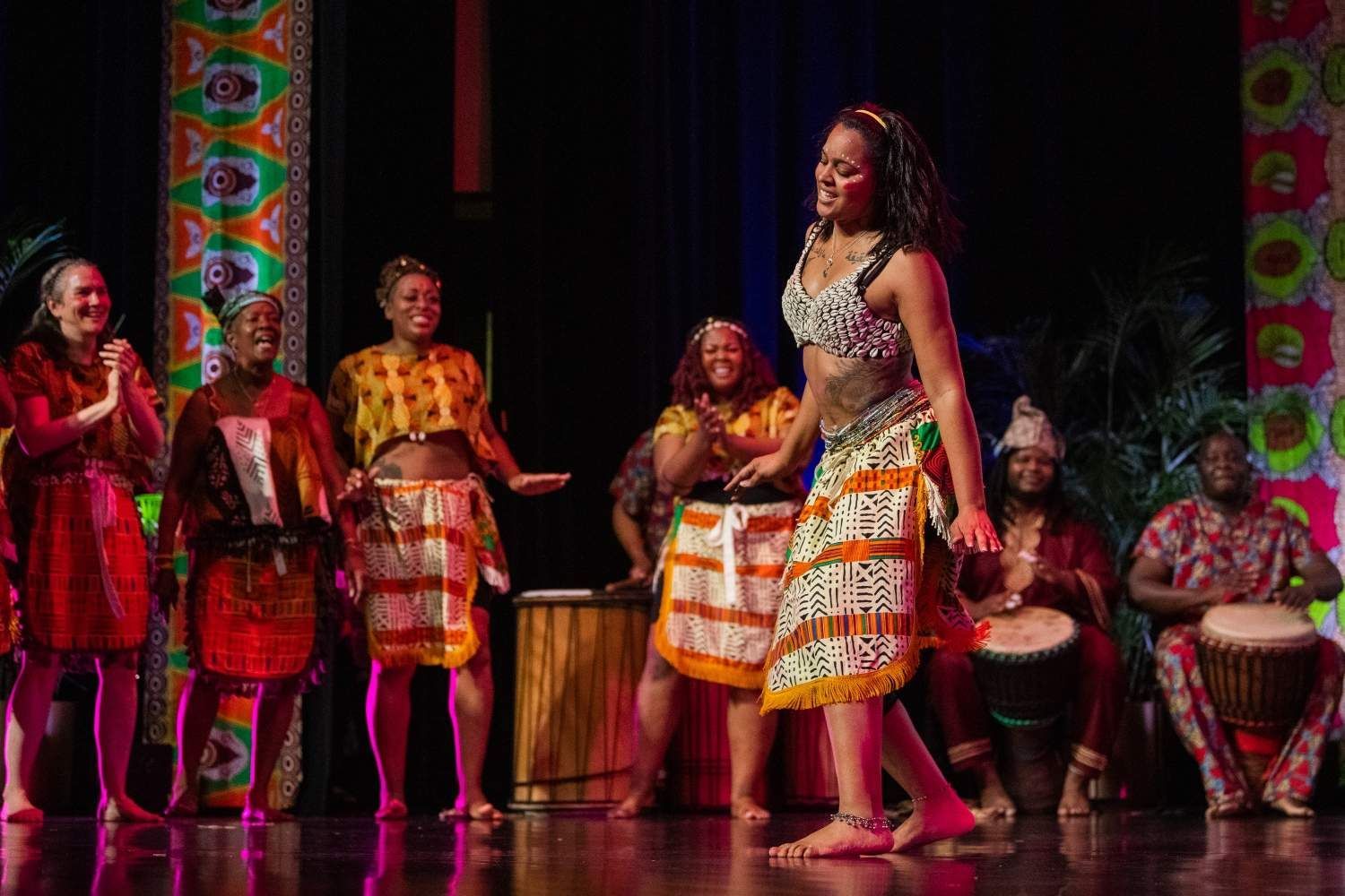 African dancers and musicians on a stage. Bright costumes, colorful backdrop. Celebrating a cultural performance.