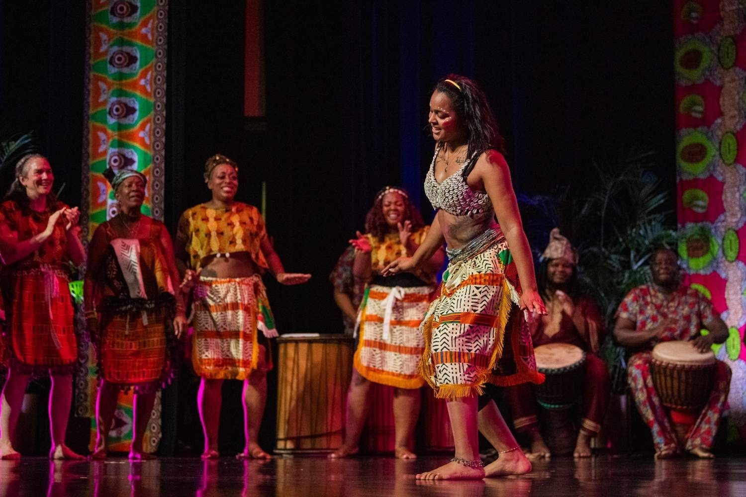 African dancers on stage, colorful costumes, drums, musicians, lively performance.