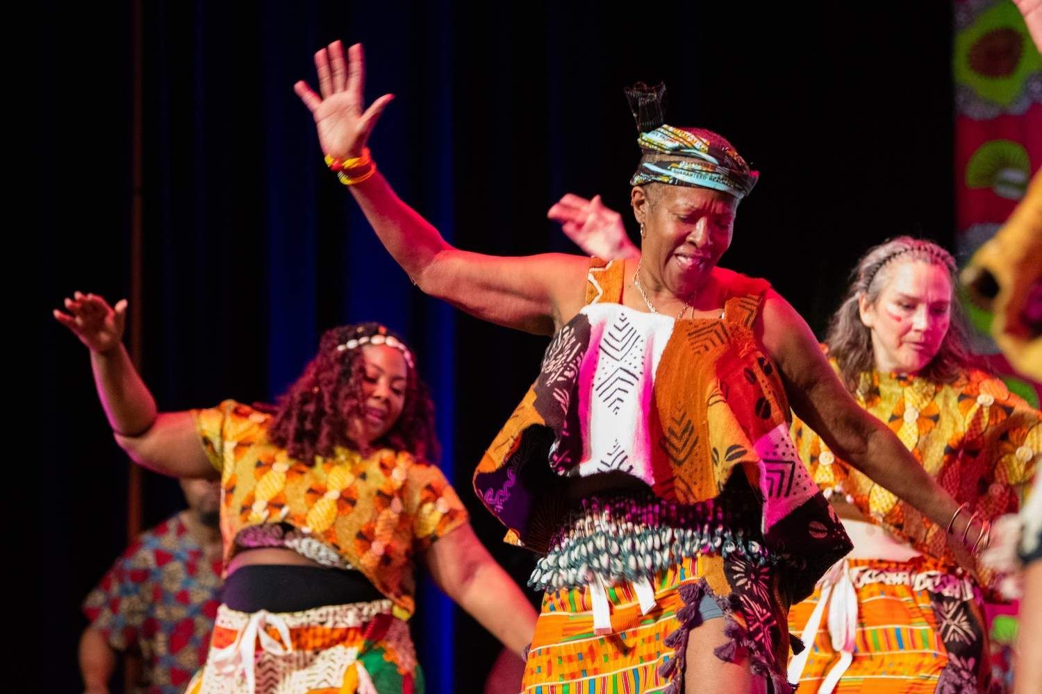 Dancers in colorful African attire performing onstage, raising arms.