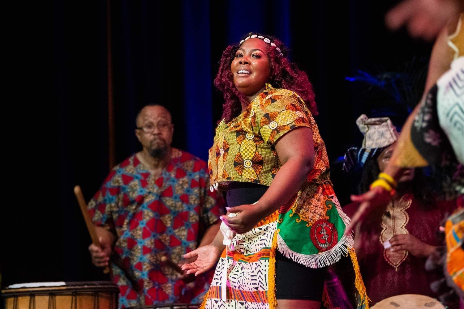 Woman in African print outfit dances onstage, band in background.