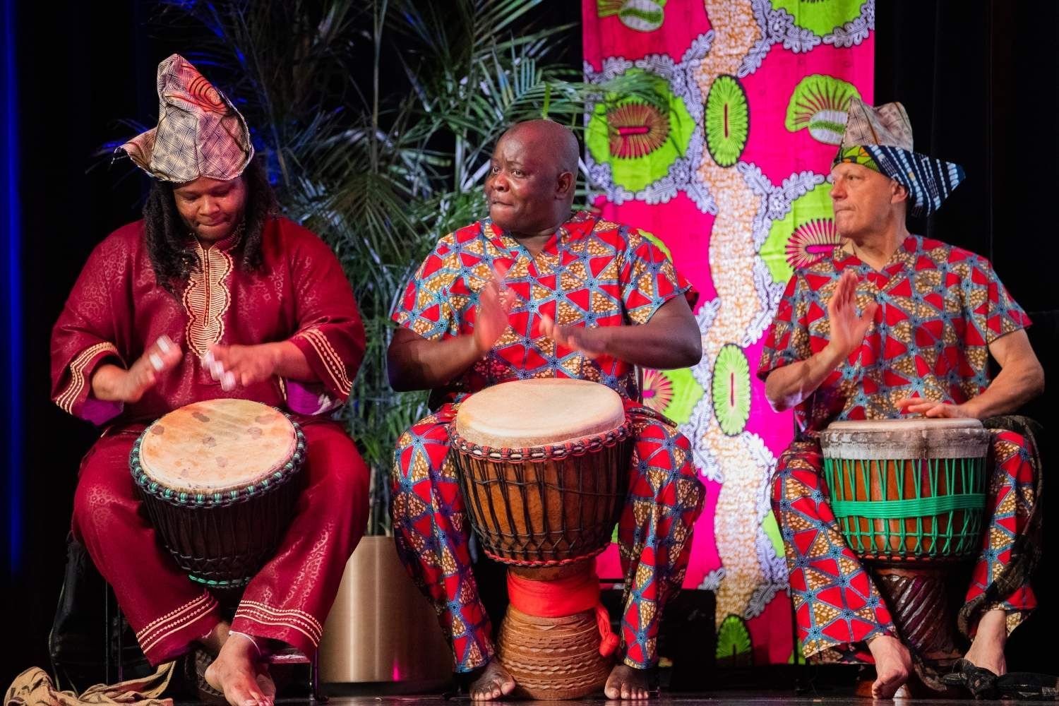 Three people in African attire play drums onstage.