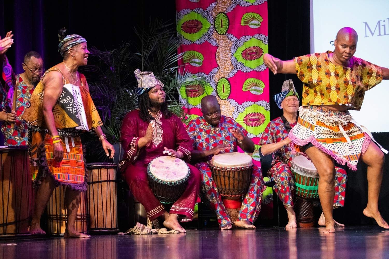 African drummers and dancers on stage, vibrant colorful clothing, lively performance.