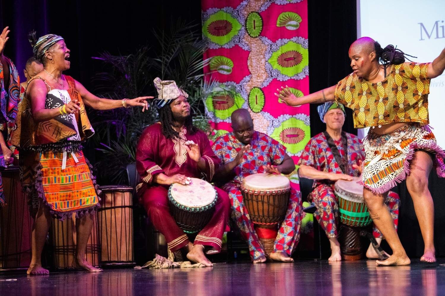African drummers and dancers performing onstage; bright colors and expressive movements.