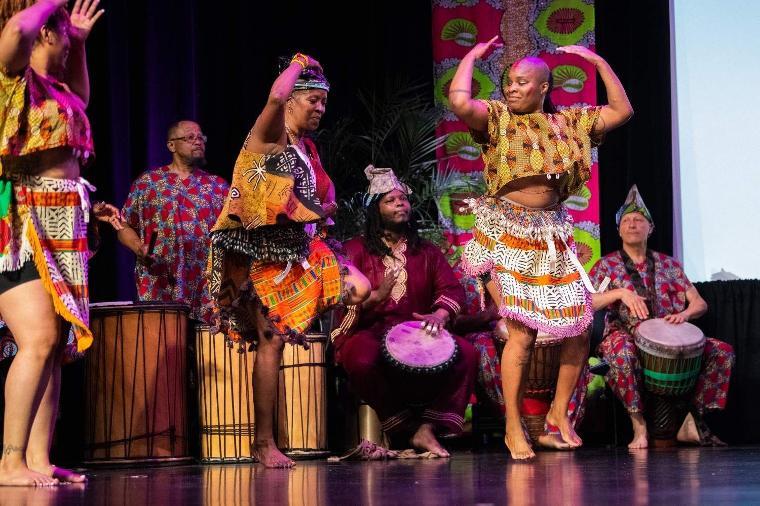 African dancers and drummers on stage; vibrant costumes, movement, and music.
