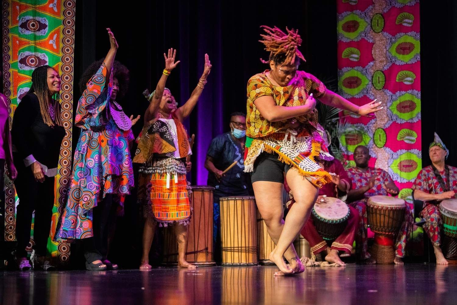 People dancing onstage with drums, wearing colorful African-inspired clothing.