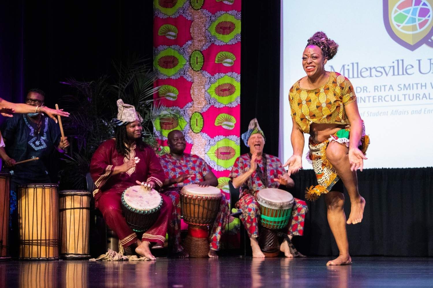 A woman dances barefoot on stage with drummers in colorful African clothing at Millersville University.