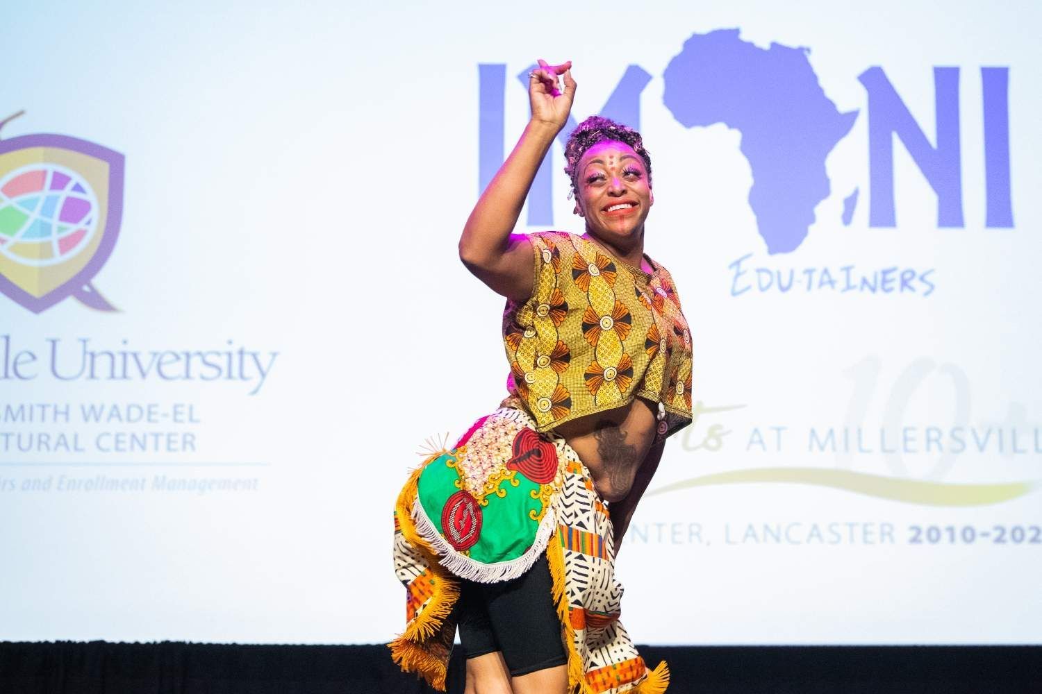 Woman in African-print outfit dancing on stage with a map of Africa in the background.