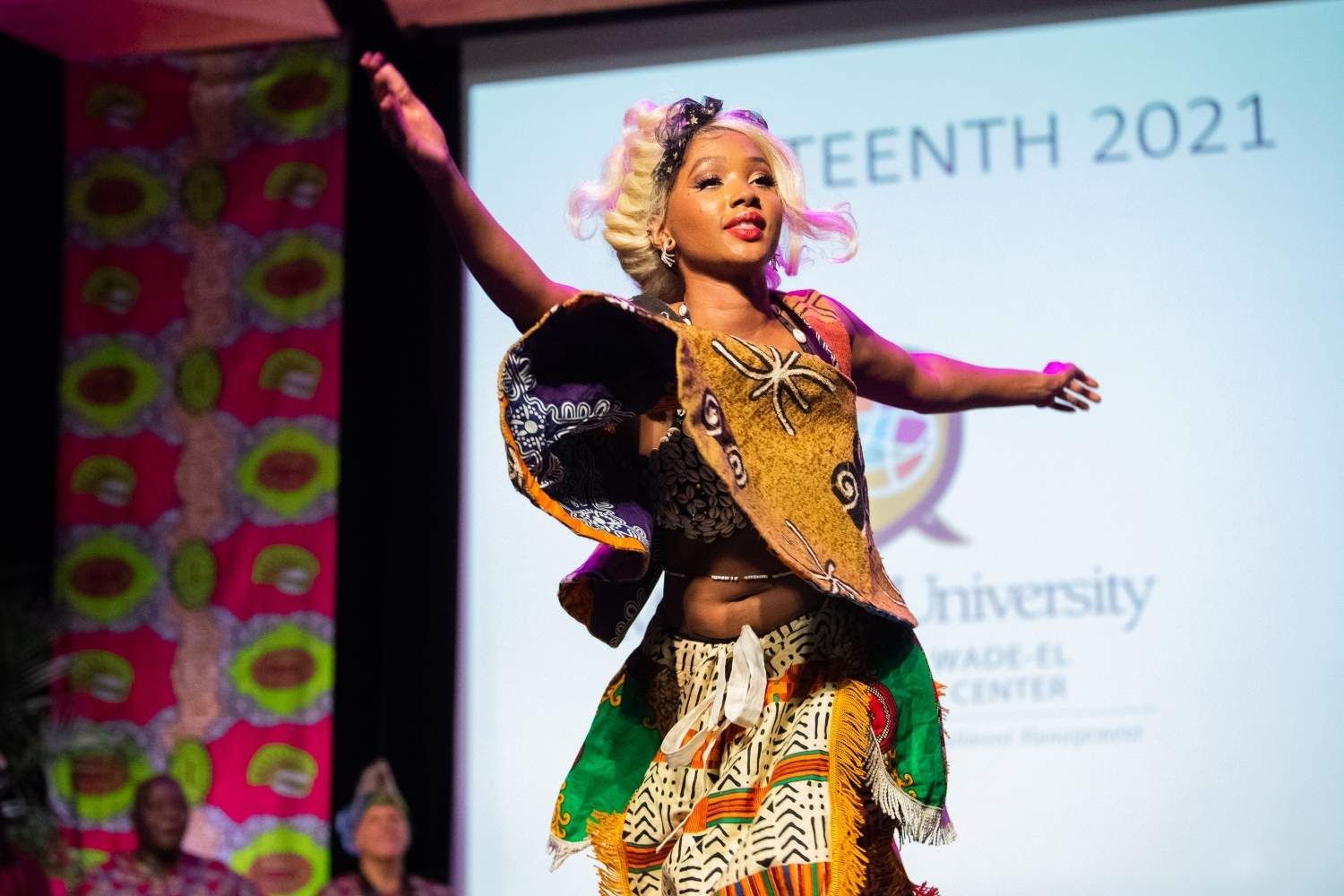 Woman in African-inspired dress dancing on stage, arms outstretched, during a Juneteenth event.