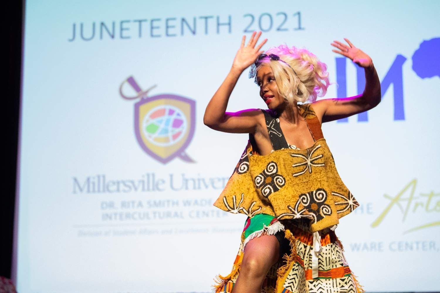 Woman dancing on stage at Juneteenth event, wearing colorful patterned dress.