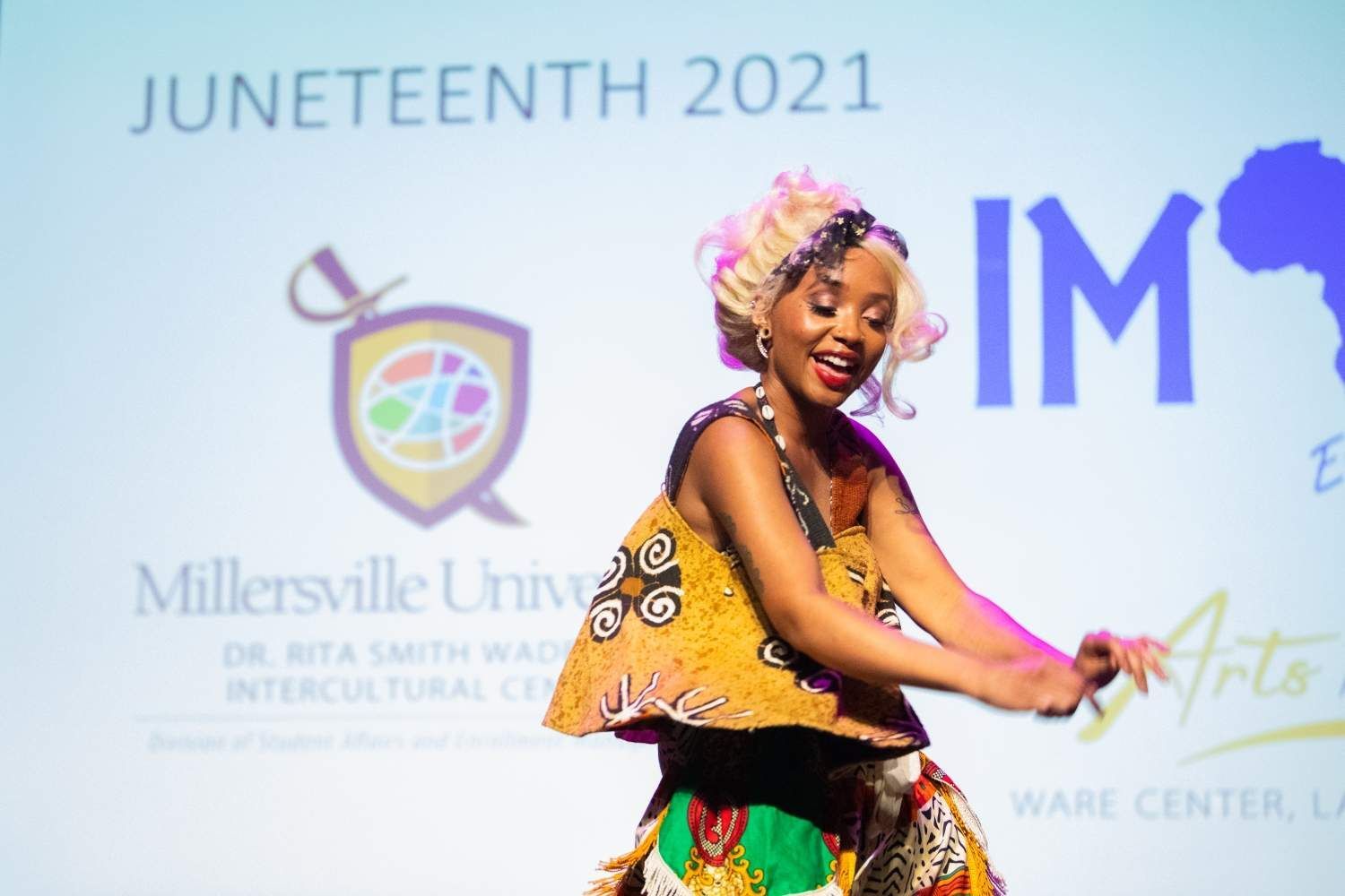 Woman in African attire dances on stage at Juneteenth event.