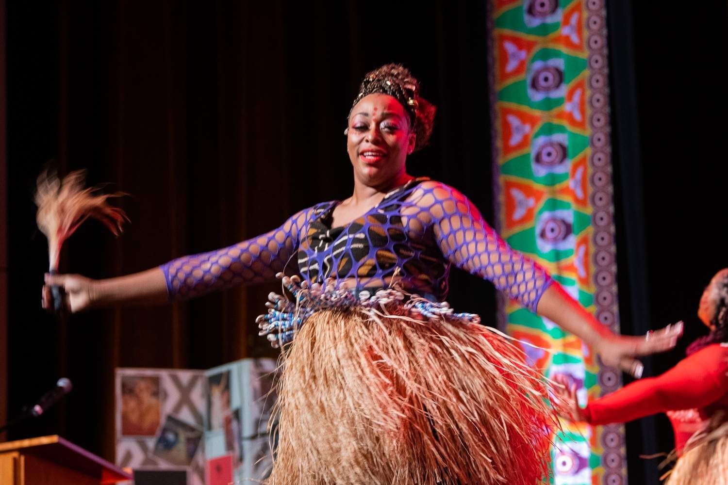 Woman in cultural attire dancing on stage with arms outstretched.