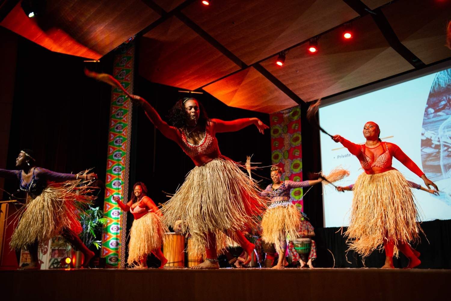 Dancers on stage in traditional African dress. Lit by red and orange light.
