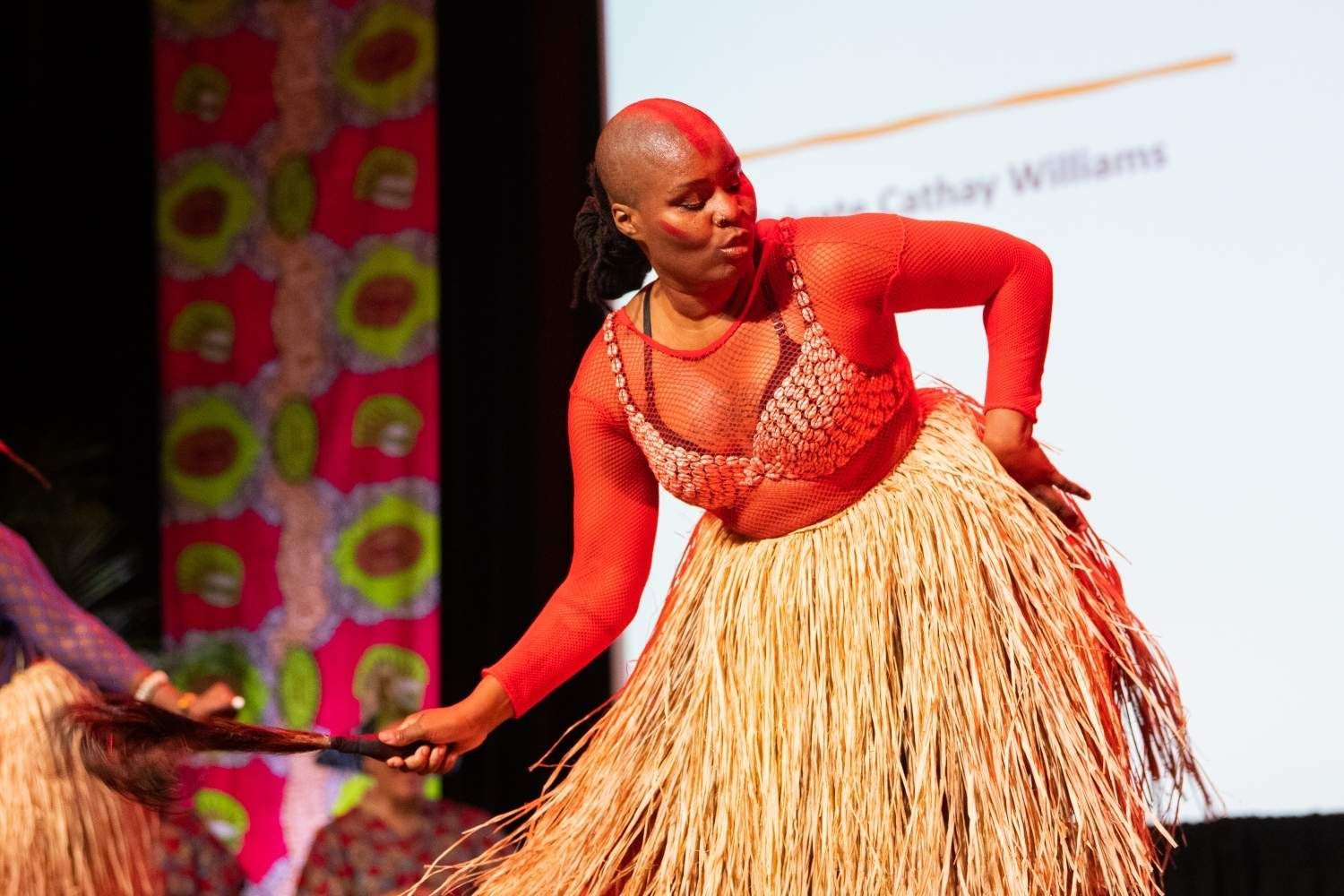 Woman in red top and straw skirt dancing on stage.