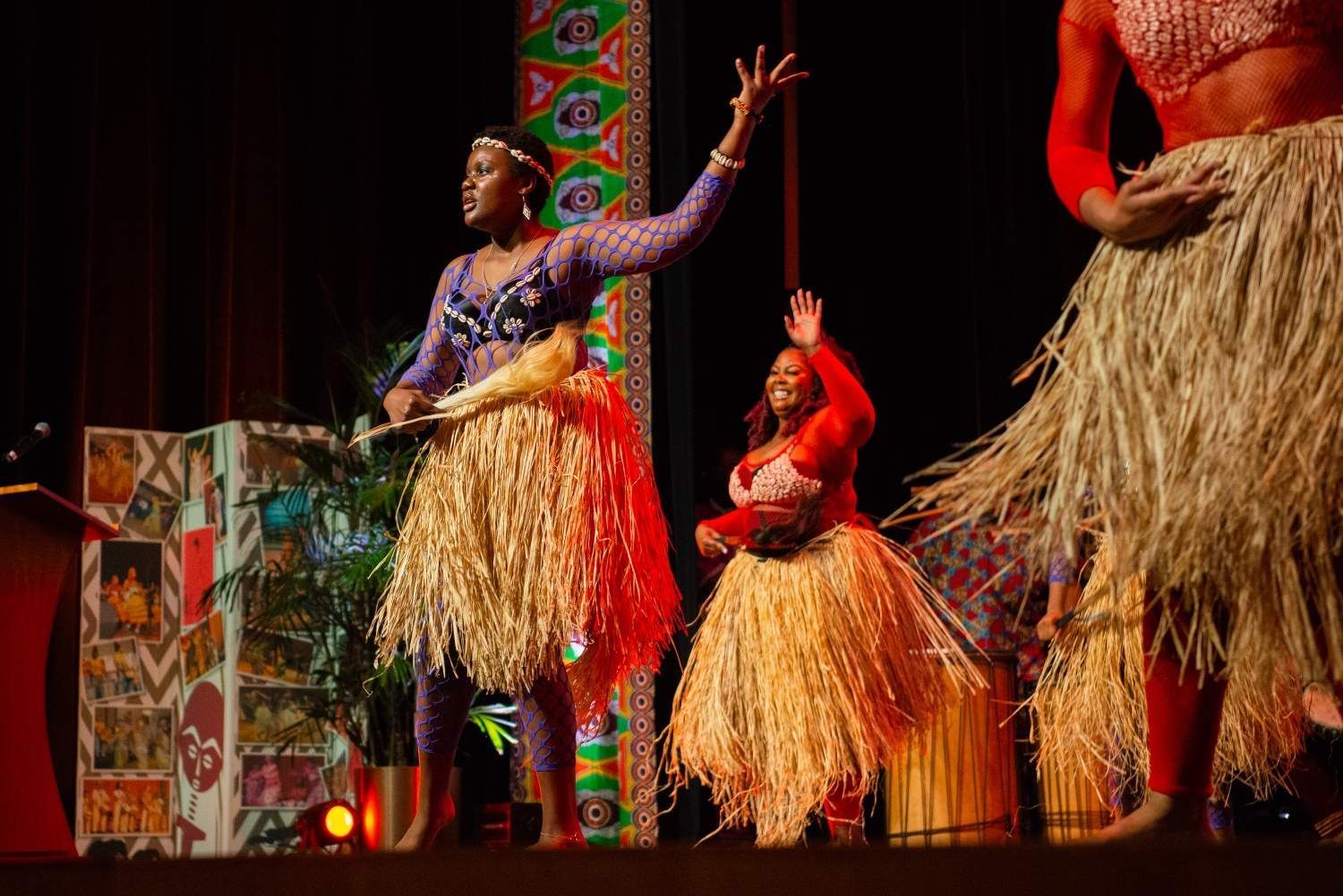 Three people on stage in vibrant costumes perform a dance.