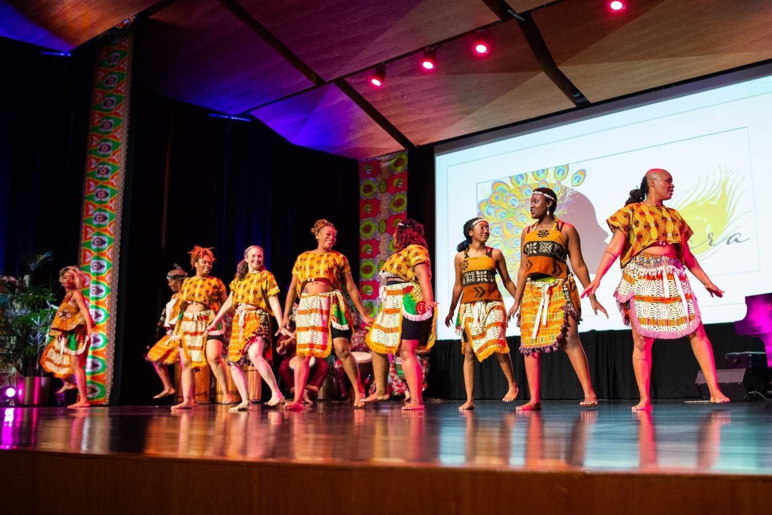 A group of dancers in vibrant African attire perform on stage under stage lights.