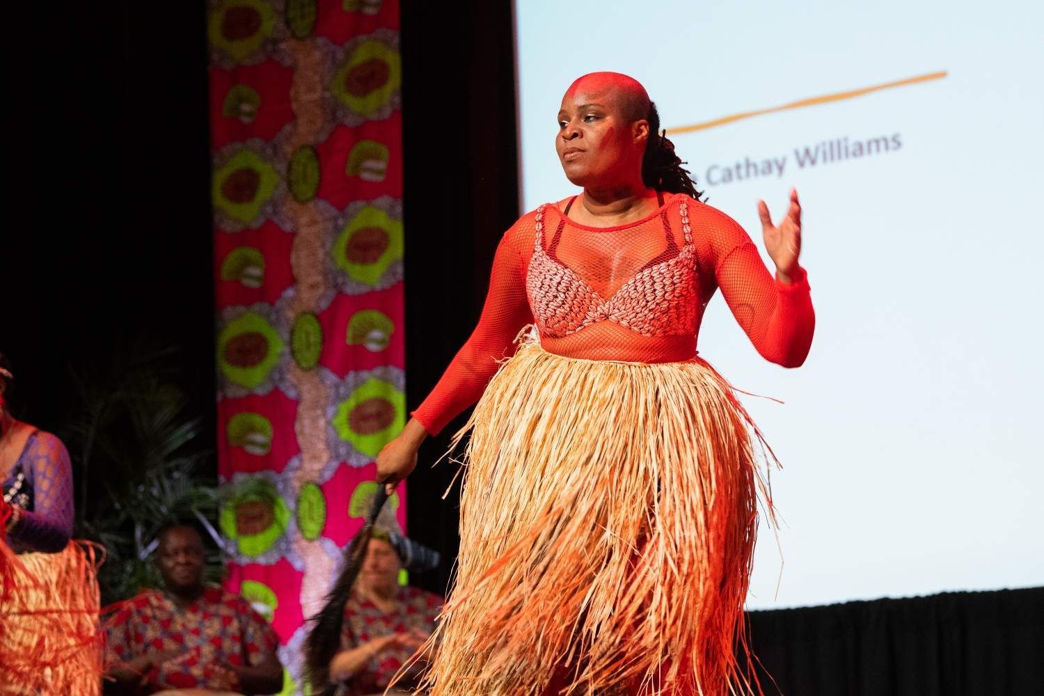 Woman in red outfit with straw skirt performs on stage.