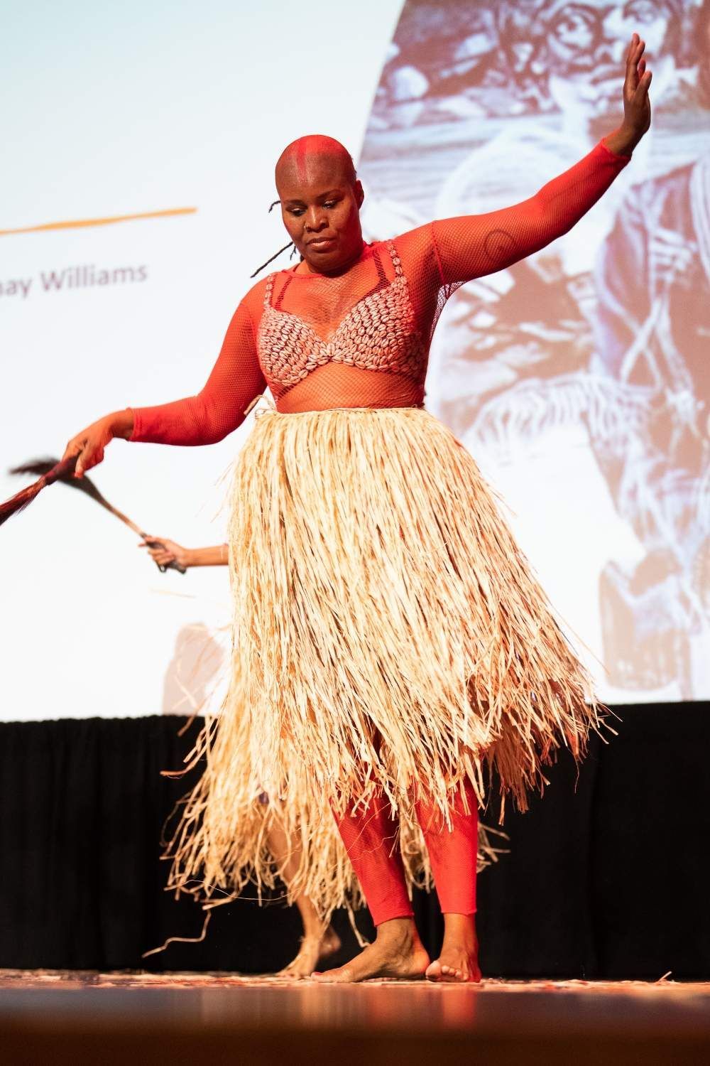 Woman in red outfit and grass skirt dances on a stage.