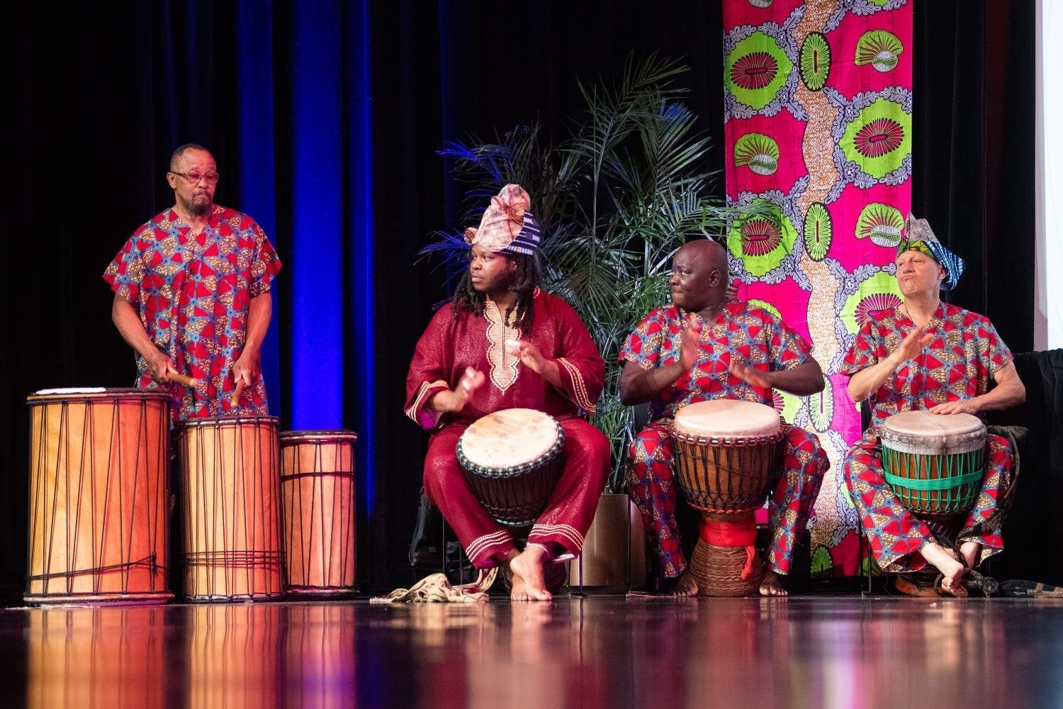 Four people in colorful African attire playing drums on stage.