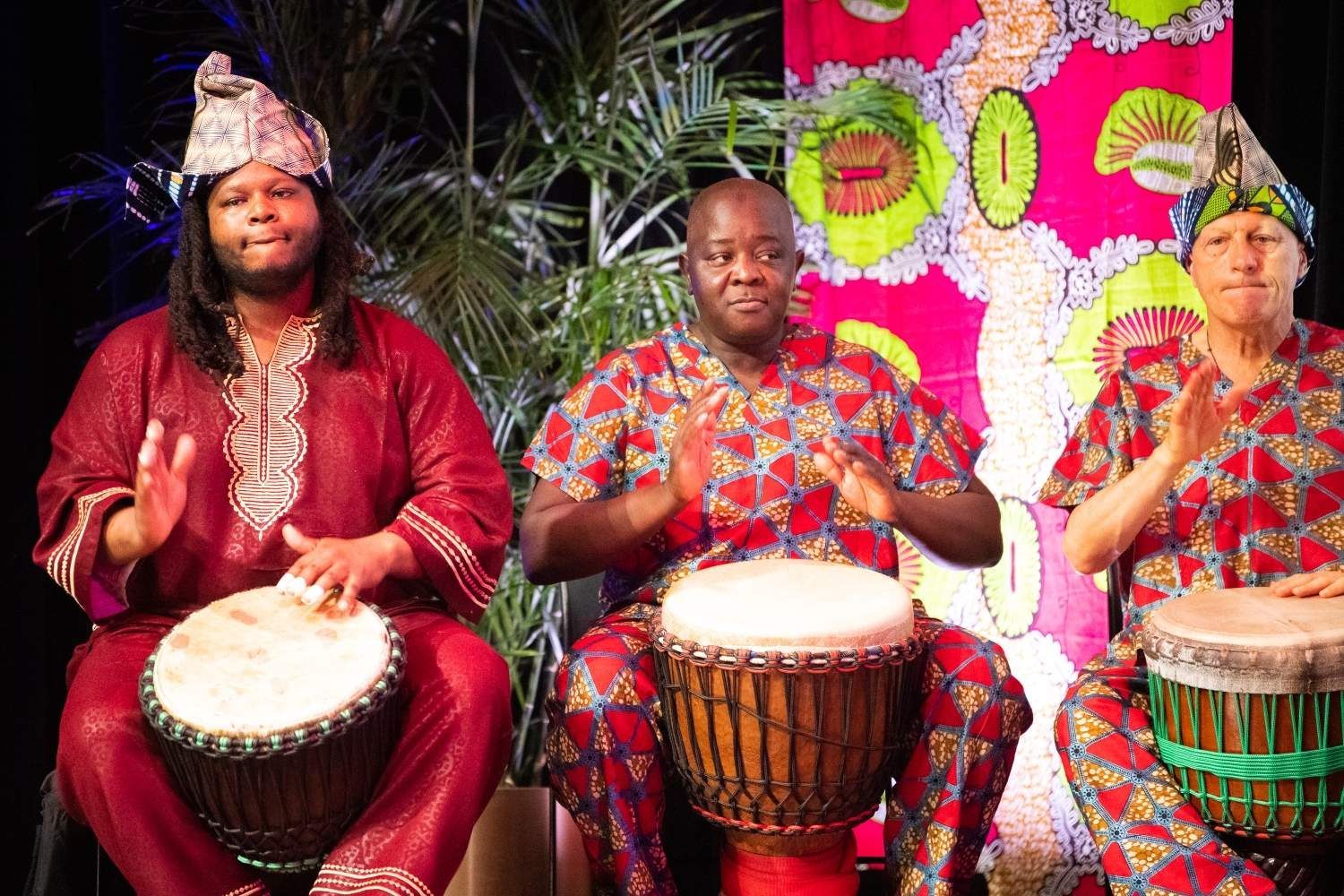Three people in colorful African attire playing drums.