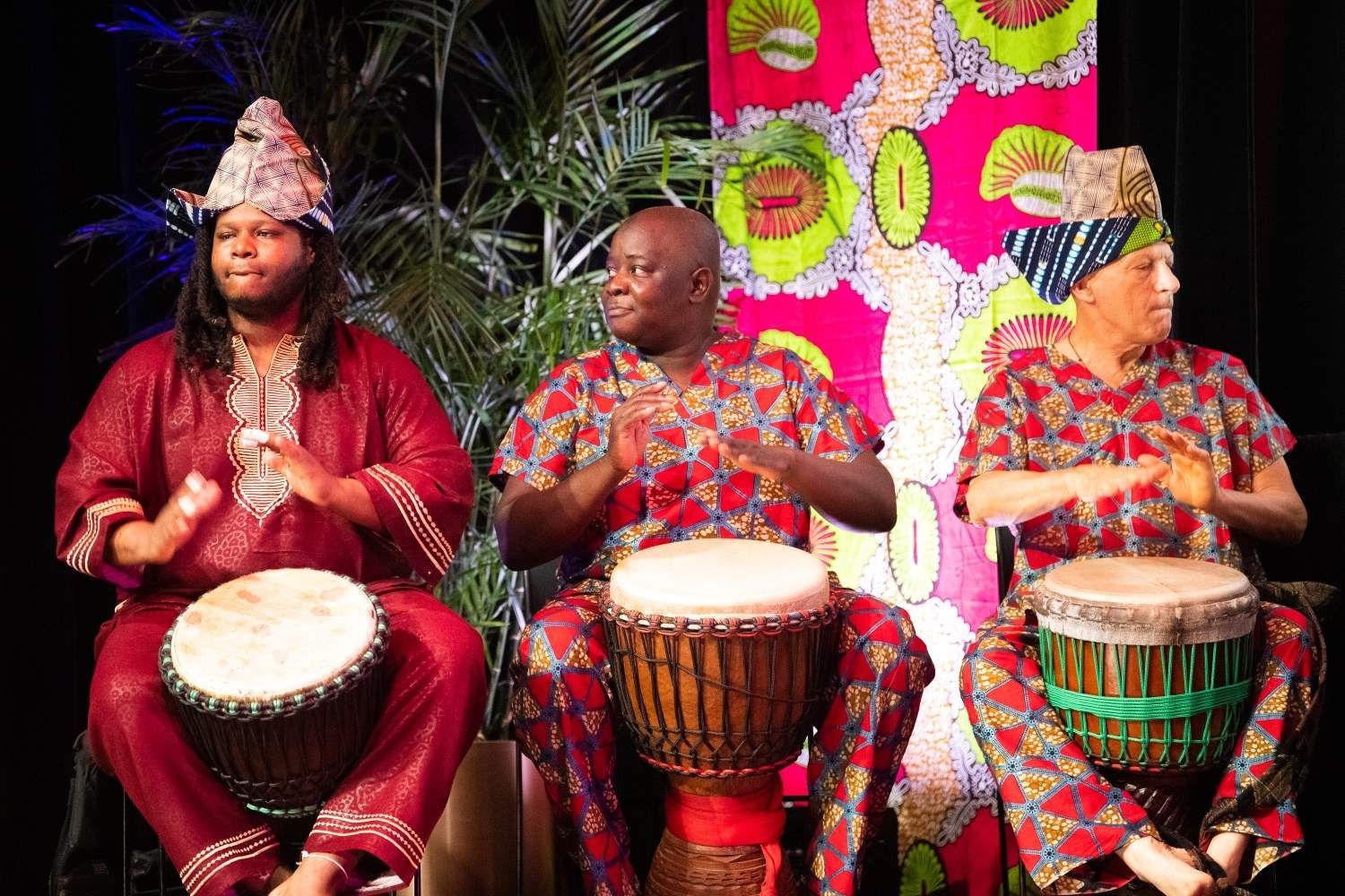 Three people in colorful African attire playing drums.