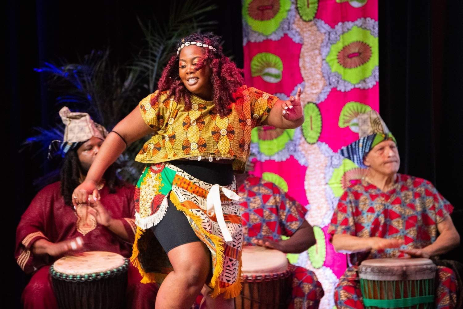 Woman dancing in colorful African attire with drummers on stage.